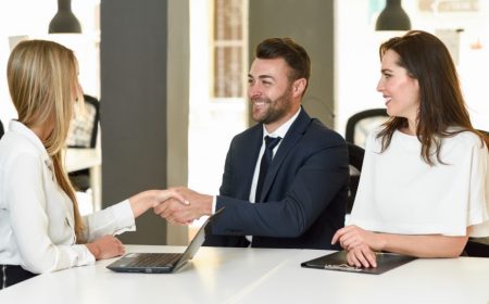 Smiling young couple shaking hands with an insurance agent or investment adviser. Three people meeting in an office reaching an agreement